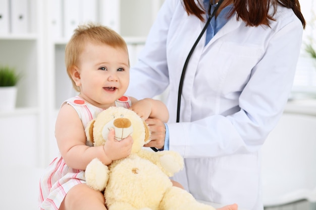 Photo pediatrician is taking care of baby in hospital little girl is being examining by doctor with stethoscope health care insurance and help concept