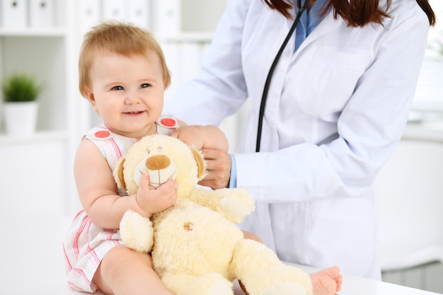 Photo pediatrician is taking care of baby in hospital little girl is being examining by doctor with stethoscope health care insurance and help concept