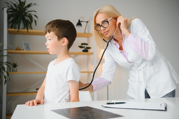 Pediatrician listening to breathing in the lungs and heartbeat with stethoscope Portrait of adorable little boy visiting doctor