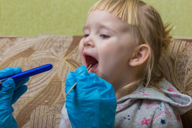 The pediatrician looks at the throat of a sick girl Home visit