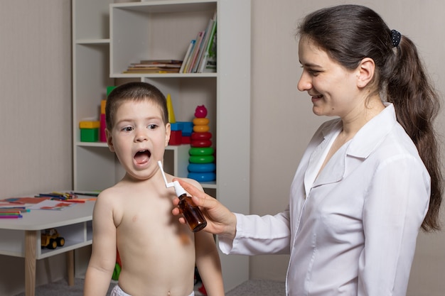 The pediatrician puffs throat spray into the boy's mouth.