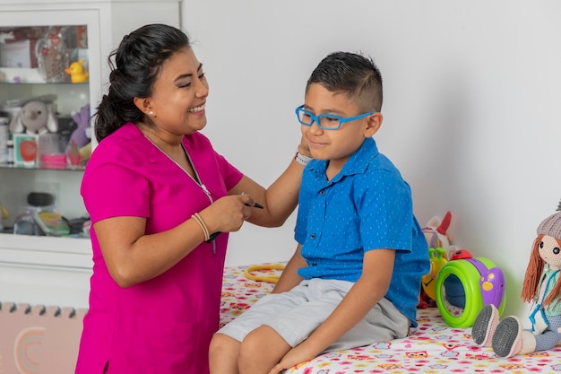 Pediatrician woman smiling while checking on a child who is sitting on the bed in her office