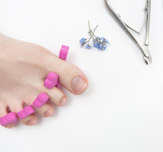 Pedicure of the feet with separators of naked nails on a white background with small lilac flowers