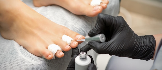 Pedicurist applying transparent varnish to the female toenails in a beauty salon.