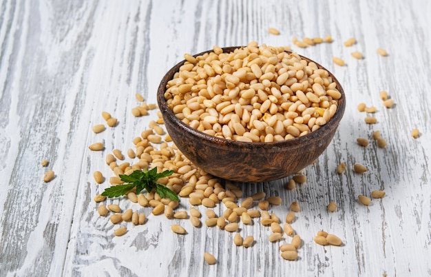 Peeled cedar nuts in a wooden cup on a white wooden background Rustic style The concept of vegetarian and diet snacks