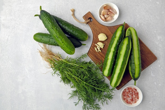 Peeled fresh cucumbers on a brown wooden cutting board with a bunch of dill garlic and pink salt