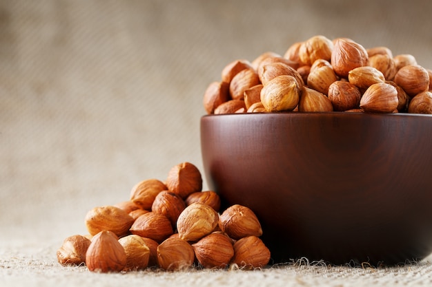 Peeled hazelnuts in a wooden, dark brown cup on a burlap cloth