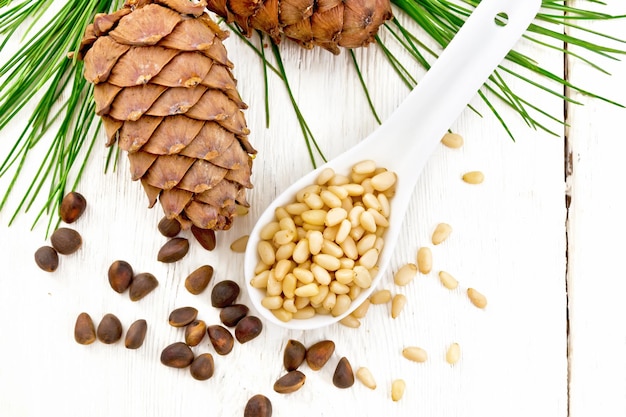 Peeled kernels of cedar nuts in a spoon two pinecones and nuts in the shell against a light wooden board on topxA