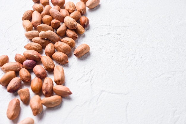 Peeled peanuts on white concrete textured background side view selective focus close up space for text.