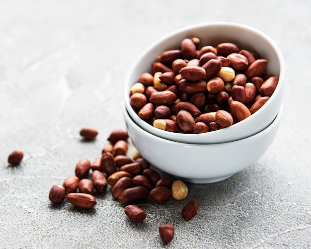 Peeled peanuts in a wooden bowl on a grey concrete background