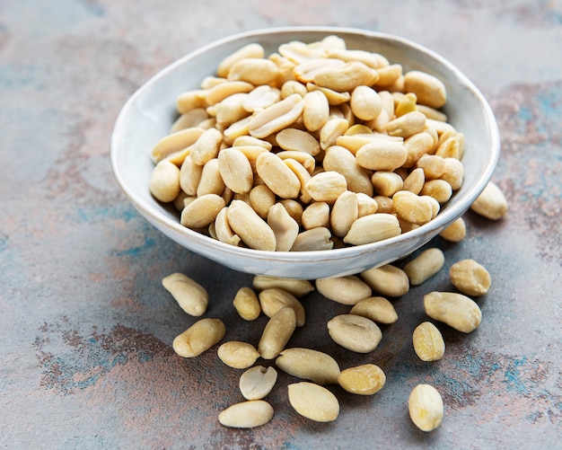 Peeled peanuts in a wooden bowl on a grey concrete surface