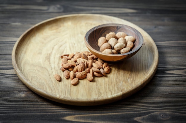 Peeled raw almonds on a wooden plate and almonds in a shell in a wooden bowl on a wooden background