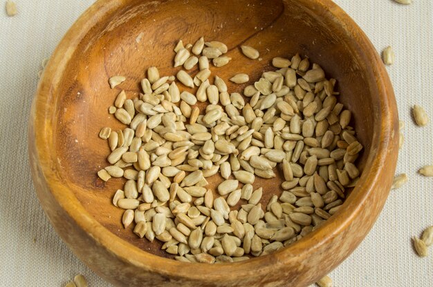 Peeled sunflower seeds in old wooden bowl on white cloth