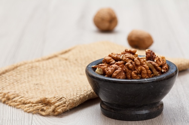 Peeled walnuts in stone bowl with sackcloth on a wooden background. Useful nutritious protein product. Shallow depth of field.