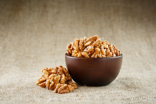 Peeled walnuts in a wooden, dark brown cup on a burlap cloth