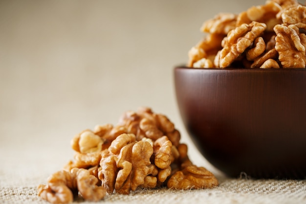 Peeled walnuts in a wooden, dark brown cup on a burlap cloth