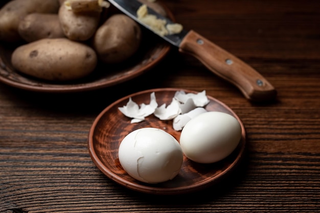 Peeling chicken eggs on a dark wooden background In the background out of focus boiled unpeeled potatoes