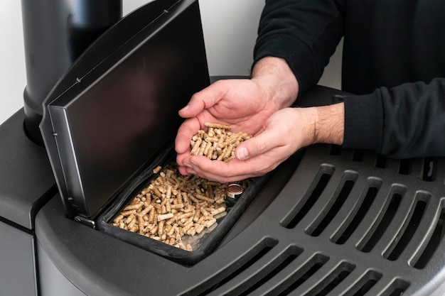 Pellet stove man holding granules in his hand above a modern black stove