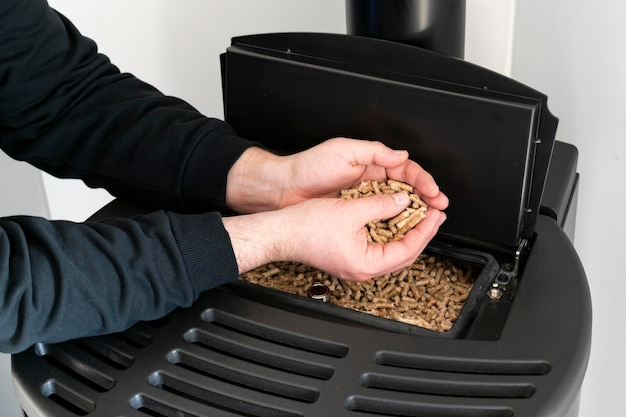 Pellet stove man holding granules in his hand above a modern black stove