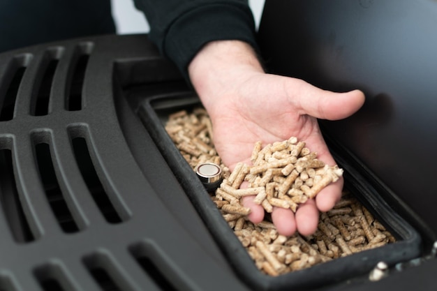 Pellet stove man holding granules in his hand above a modern black stove