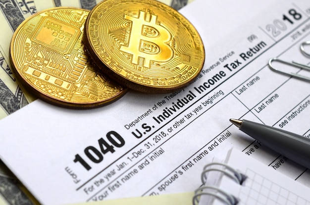 The pen, bitcoins and dollar bills is lies on the tax form 1040 U.S. Individual Income Tax Return. The time to pay taxes