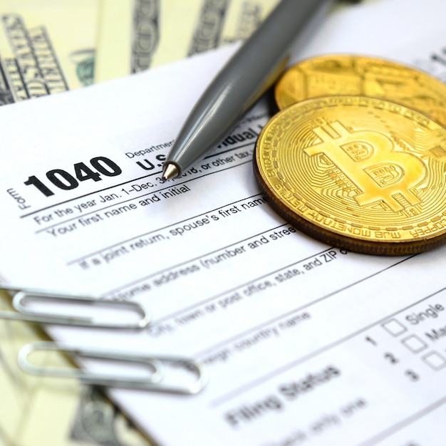 The pen, bitcoins and dollar bills is lies on the tax form 1040 U.S. 