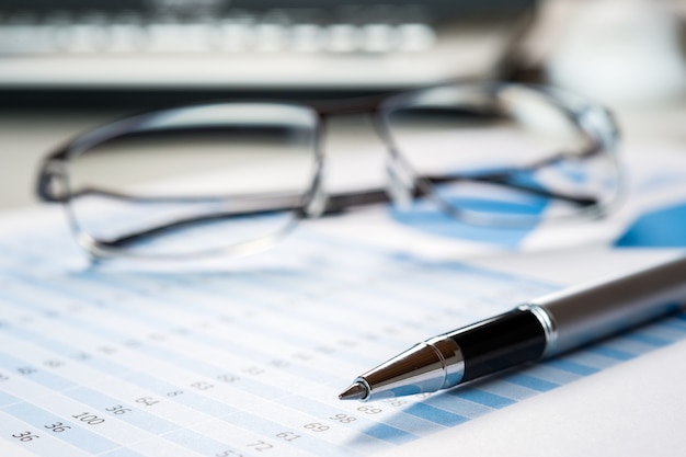 Pen and eyeglasses on financial documents, business and finance concept