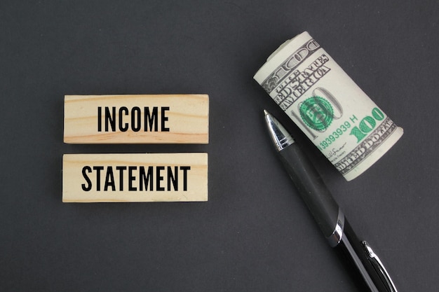 a pen, a roll of paper money and a stick with the word Income Statement