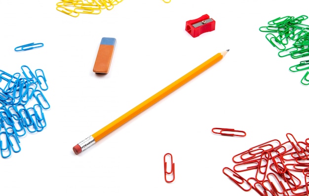 Pencil, eraser, sharpener, paper clips lie in different angles of the sheet on a white background. Hero image and copy space.