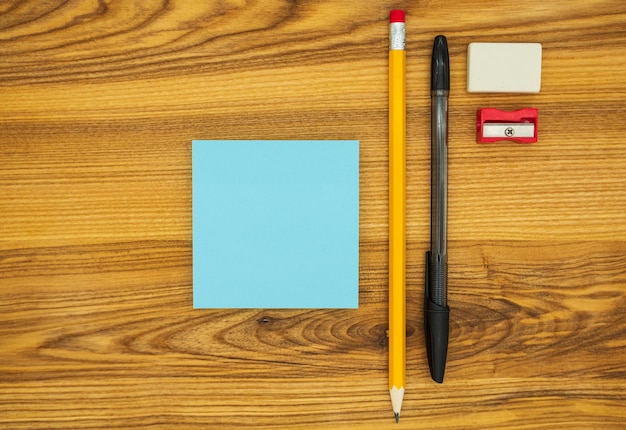 Pencil, pen, scraper, eraser and blue blank sticky notes, on a wooden desk