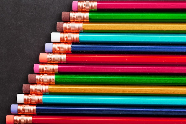 Pencils of different colors in a row on a black textured background.