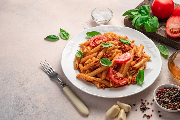 Penne pasta with bolognese sauce, a traditional Italian dish on a light background. Side view, copy space.