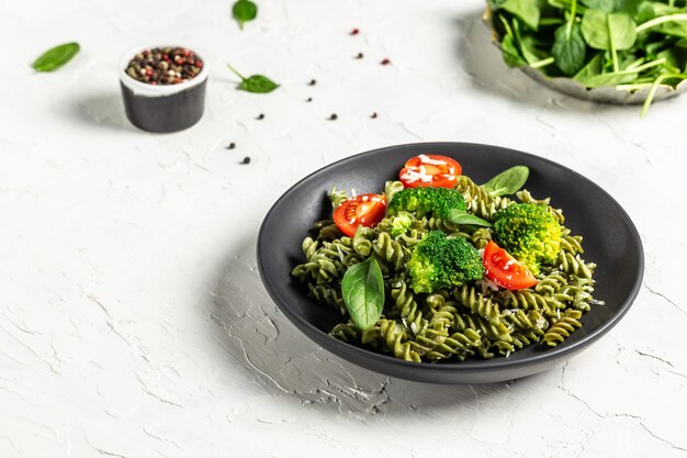 Penne pasta with broccoli, avocado sauce, spinach leaves and cherry tomatoes on liht surface.