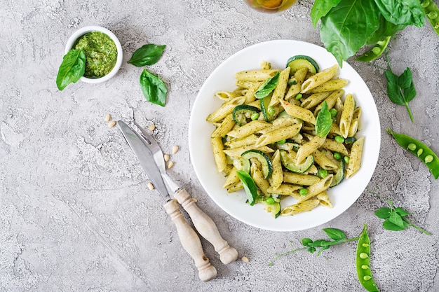 Photo penne pasta with  pesto sauce, zucchini, green peas and basil. italian food.