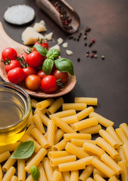 Penne pasta with tomatoes in wooden bowl with oil and parmesan cheese with salt on dark brown background Top view