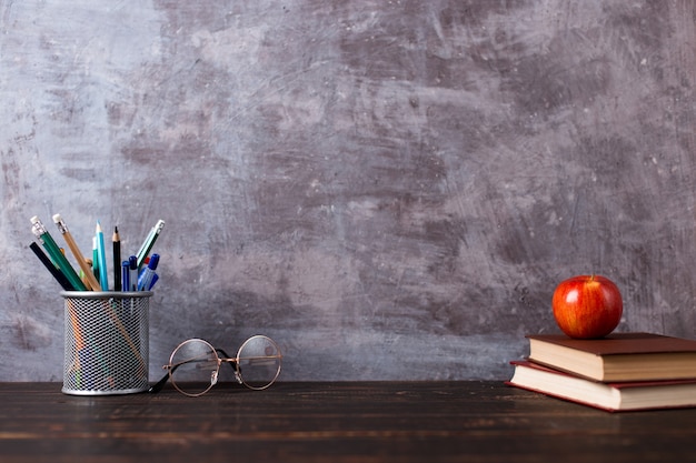 Pens, apple, pencils, books and glasses on the table