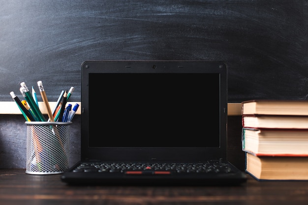 Pens, apple, pencils, books, laptop and glasses on the table, on chalkboard background