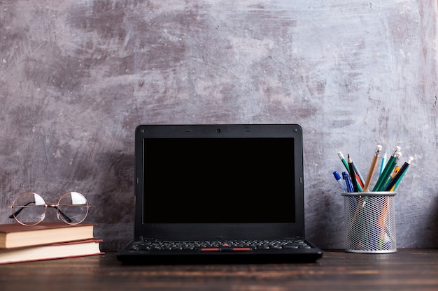 Pens, apple, pencils, books, laptop and glasses on the table, on chalkboard background