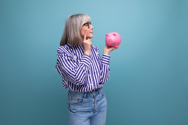 Pension contribution s middle aged woman with gray hair holding a piggy bank against a bright studio