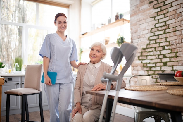 Pensioner sitting at the table near her pleasant nurse