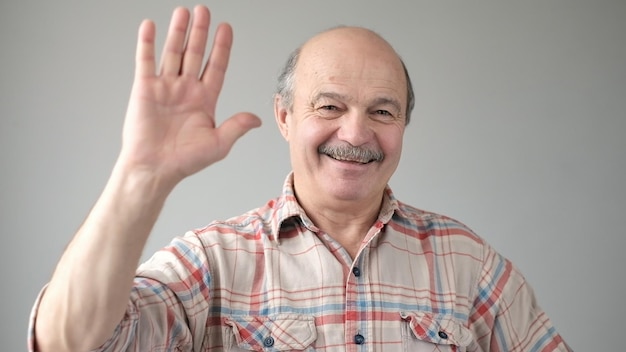 Pensioner waves hand in hello gesture while smiling cheerfully