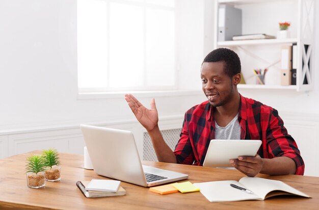 Pensive african-american businessman in office working with laptop and digital tablet, copy space