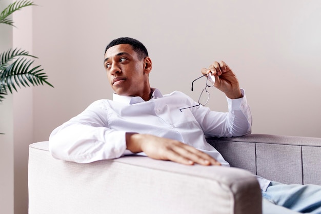 Photo pensive african american man in glasses and shirt sits in an easy chair and looks to the side