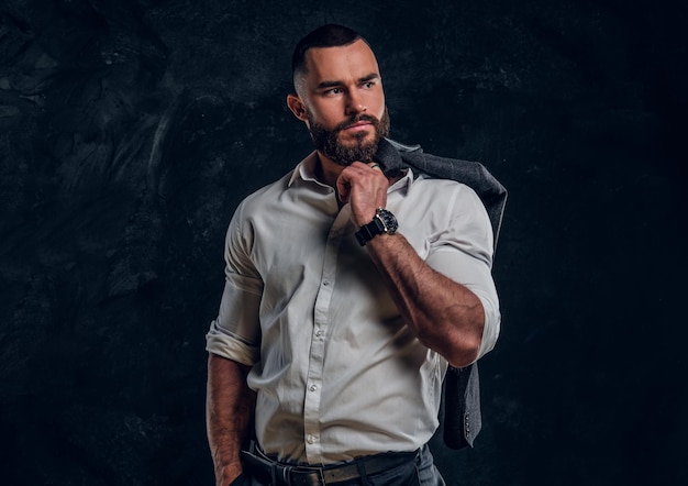 Pensive bearded businessman in white shirt is posing for photographer over dark background.