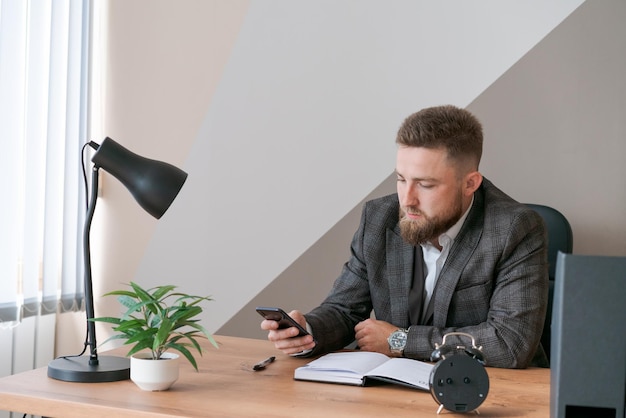 Pensive bearded young man calling by smartphones and writing down notes