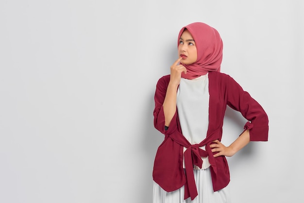 Pensive beautiful Asian woman in casual shirt thinking about something and looking away isolated over white background