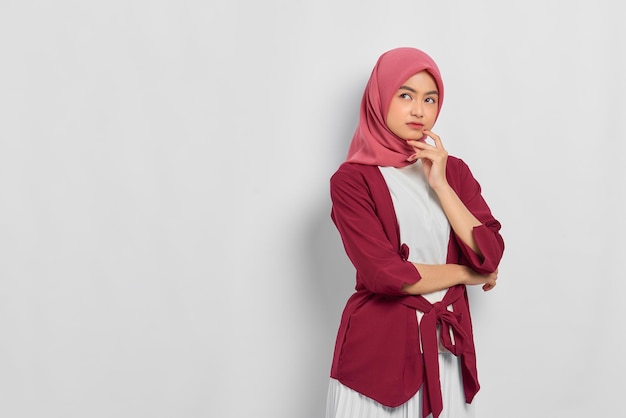 Pensive beautiful Asian woman in casual shirt thinking about something and looking away isolated over white background