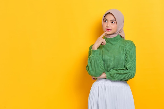 Pensive beautiful Asian woman in green sweater thinking about something and looking away isolated over white background