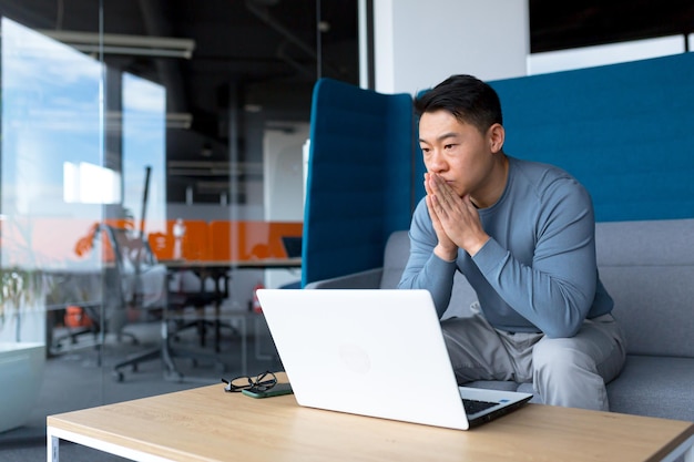 Pensive businessman in modern office working on laptop asian boss makes difficult choice