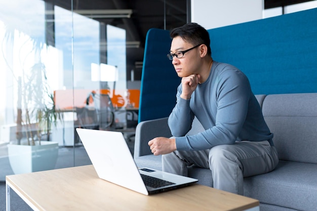 Pensive businessman in modern office working on laptop asian boss makes difficult choice